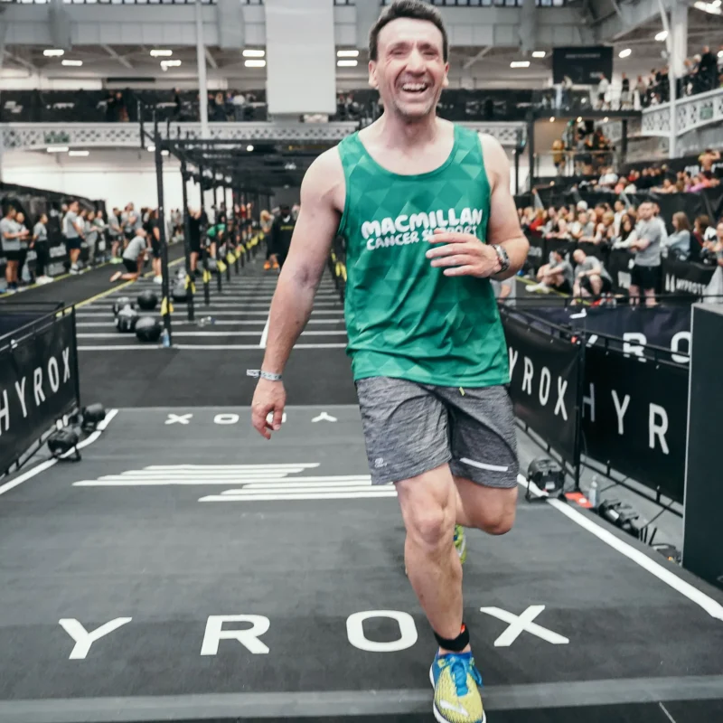 Richard Branson crosses the finish line of solo hyrox event wearing Macmillan top