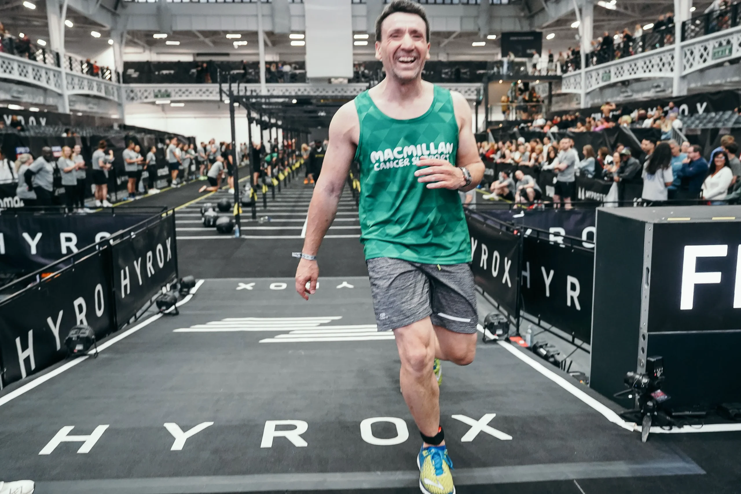 Richard Branson crosses the finish line of solo hyrox event wearing Macmillan top